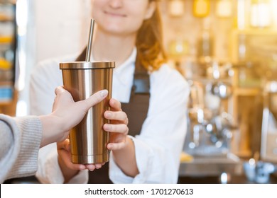Closeup female hands are holding metal reusable tumbler cup mug of coffee. Woman  prepared, brewed espresso, americano, latte cappuccino in cafe. Barista is giving order to client. Take away, to go.