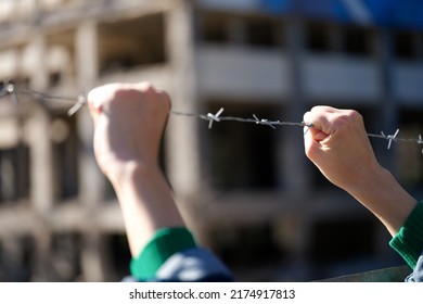 Close-up of female hands holding security barbedwire fence, wire with clusters of short, sharp spikes. Fence or warfare obstruction, correctional institution concept