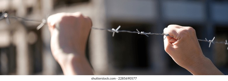 Close-up of female hands holding security barbedwire fence, wire with clusters of short, sharp spikes. Fence or warfare obstruction, correctional institution concept