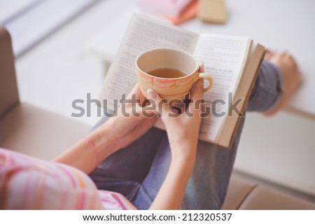 Close-up of female hands holding teacup in front of opened book