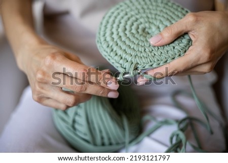Closeup female hands knitting interior decor basket use green ribbon yarn and crochet needle. Creative woman arms enjoying needlecraft hobby or art work making comfortable cotton sewing accessories