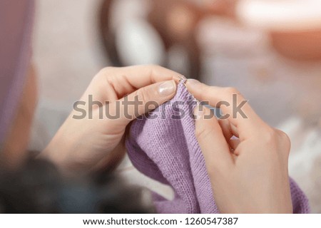 Close-up female hands knitting outdoors. Woman knitting in park during walk with baby in stroller. Process of needlework.