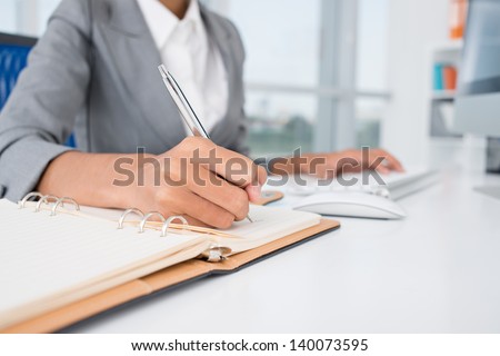 Close-up of female hands making notes in the notepad at office