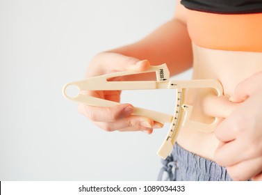 Close-up Of Female Hands Measuring Fat Belly With Fat Caliper by herself in black orange sport bar