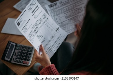 Close-up of female hands with pay slips, utility bills, account statements, payment receipts. A woman makes a count of household, family expenses with a calculator at home on the table.