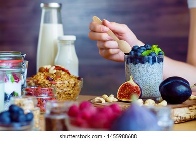 Closeup female hands are preparing organic yogurt with chia for good digestion, functioning of gastrointestinal tract. Summer berries, nuts, fruits, dairy products on table. Healthy food concept.
