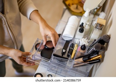 Closeup female hands putting luxury cosmetic into acrylic box with drawer storage organization. Beauty products tidying up neatly placement at minimalist container. Powder, foundation, lipstick, blush