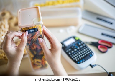 Closeup Female Hands Sticking Label On Plastic Package With Pasta. Storage Organization Of Food Products Keeping. Woman Doing Housework Organize Use Electronic Typing Title Name Case Box