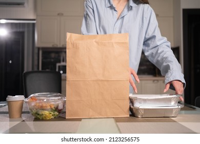 Close-up Of Female Hands Take Out Food In Disposable Trays From A Paper Bag And Put It On The Table. Unpacking An Order From A Restaurant. Faceless. Copy Space