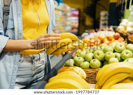 Close-up of female hands taking bananas from the store shelf, healthy food, shopping for groceries.