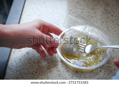 Close-up of female hands using a fork to take a pickled herring rollmops in oil, presenting a traditional preserved fish dish and classic food preparation concept.