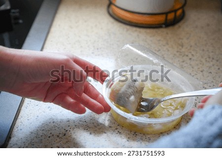 Close-up of female hands using a fork to take a pickled herring rollmops in oil, presenting a traditional preserved fish dish and classic food preparation concept.