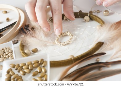 Close-up Of Female Hands With Wooden Beads, Having Dream Catcher Assembled. Handmade Workshop Composition Of Feathers, Beads, Threads, Tools For DIY  