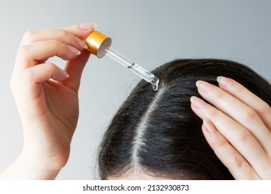Close-up of a female head with dark hair. Woman using pipette with a cosmetic product near the hair parting. The concept of dandruff.