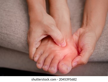 Closeup of female holding her painful feet and massaging her bunion toes to relieve pain. Swollen bunion at the edge of the big toe causes deformity (Hallux valgus). Woman's health concept. - Shutterstock ID 2045395682