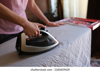 Close-up of female housewife ironing crumpled bedsheet on board using steam iron. Woman doing housework. Housekeeping and household chores concept