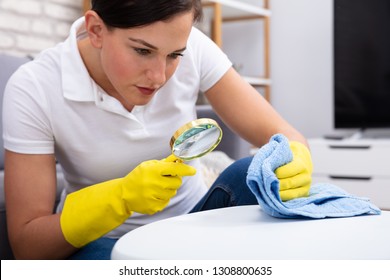 Close-up Of A Female Janitor Examine Table Using Magnifying Glass And Blue Napkin