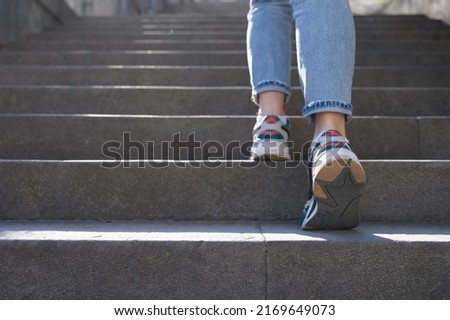 Close-up of female in jeans and sneakers going up steep stairs. Woman tourist in casual clothes going upstairs outdoors