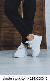 Close-up Of Female Legs In Black Jeans In Stylish Leather White Sneakers. Fashionable Woman In New Sneakers. Modern Seasonal Collection Of Stylish Sneakers. Women's Fashion.