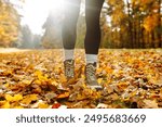 Close-up of female legs in hiking boots on autumn leaves in the park. Travel and hiking. Autumn mood.