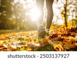 Close-up of female legs in hiking boots walks on ground with yellow-orange dry fall leaves during autumn season in park or forest. Feet walking in outdoor nature. Healthy lifestyle on leisure activity