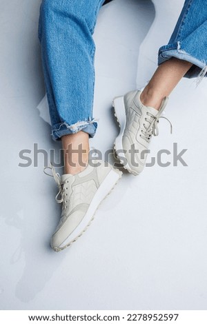 Close-up of female legs in jeans and white stylish sneakers. Casual women's fashion. Comfortable shoes for women. Women's comfortable summer shoes.