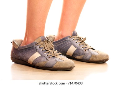 A Closeup Of Female Legs Trying On Too Big Male Shoes Over White Background