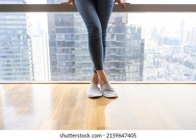 Close-up female legs ware jeans and slippers standing near full length window. relaxing after work day, comfortable living space. Copy space - Powered by Shutterstock