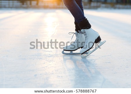 Closeup of  female legs in white old fashion skates on outdoor ice rink. Young woman skating on frozen lake in snowy winter park on sunset time
