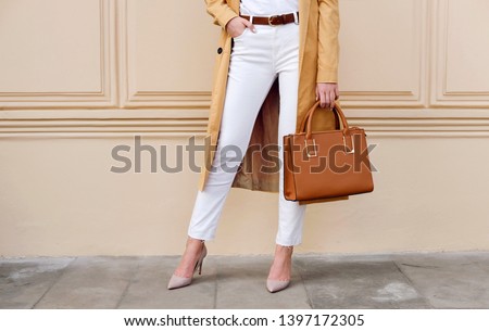Closeup female legs. Woman in coat and white jeans with brown handbag. Fashion street autumn outfit