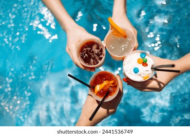 Close-up of female and male hands holding glasses with iced cocktails and clinking them. Friends make festive toast with delicious drinks against background of clear blue pool water. Party, vacation. - Powered by Shutterstock