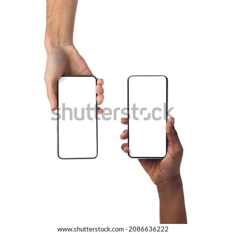 Closeup of female and male hands holding 2 smartphones with white empty screen, showing using devices, transfer data, sharing media. Two vertical gadgets with copy space, mock up, studio background