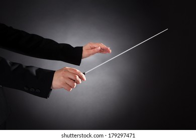 Close-up Of Female Orchestra Conductor Holding Baton Over Black Background