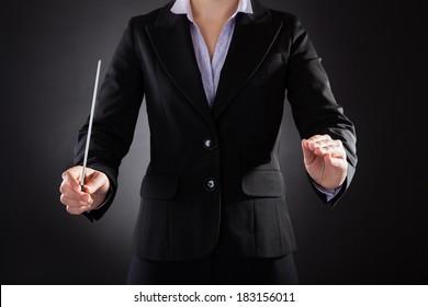 Close-up Of Female Orchestra Conductor Holding Baton Over Black Background