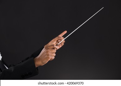 Close-up Of Female Orchestra Conductor Holding Baton Over Black Background