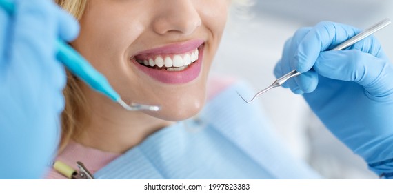 Closeup of female patient showing her beautiful white teeth while having treatment at dental clinic, dentist hands in rubber gloves holding dental tools, panorama. Woman having regular checkup - Shutterstock ID 1997823383