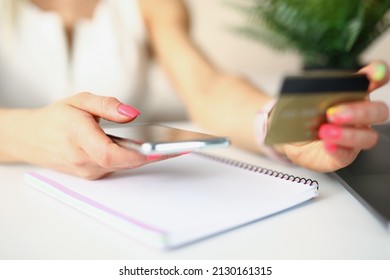 Close-up of female person paying for services or goods on smartphone with credit card. Woman using telephone. Open notebook lying on table. Payment concept