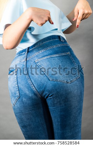 Closeup of female plus size hips buttocks wearing blue jeans, woman presenting fashionable outfit. Fashion clothing femininity concept. Gray background