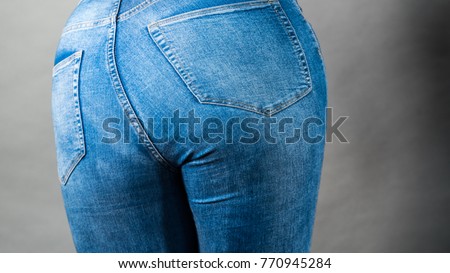 Closeup of female plus size hips buttocks wearing blue jeans, woman presenting fashionable outfit. Fashion clothing femininity concept. Gray background