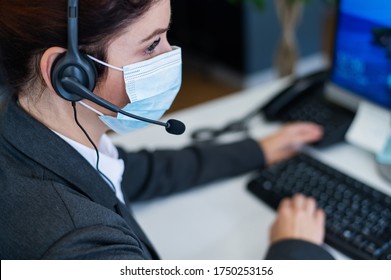 Close-up of a female receptionist wearing a facial mask talking on a headset while sitting at a work desk in the office. Portrait of a manager working during a coronavirus epidemic. - Powered by Shutterstock