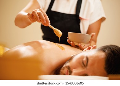 Close-up of female therapist pouring honey on man's back during massage therapy at the spa.  - Powered by Shutterstock