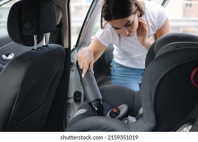 Close-up of female using a portable vacuum cleaner in her car. Baby carseat cleaning. Woman vacuuming seats. Dust and dirt removal - Powered by Shutterstock