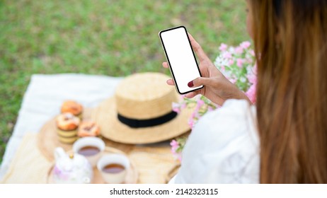 Close-up, Female using smartphone during having a nice picnic day at the green backyard. Phone white screen mockup. - Powered by Shutterstock