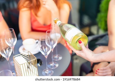Close-up female waiter holding bottle of white champagne or prosecco at outdoor party on bright summer day. Girls hen-party concept. Luxury life lifestyle. refreshing light alcoholic beverages