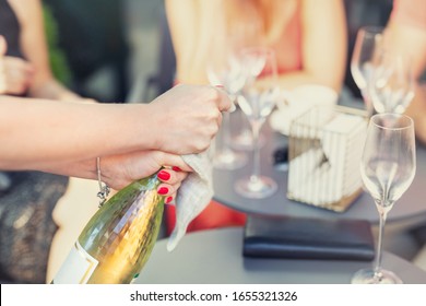 Close-up Female Waiter Opening Bottle Of White Champagne Or Prosecco At Outdoor Party On Bright Summer Day. Girls Hen-party Concept. Luxury Life Lifestyle. Refreshing Light Alcoholic Beverages