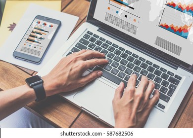 Close-up Of Female's Hands On Laptop Keyboard. Next On Wooden Table Is Smartphone With Graphs, Charts And Diagrams On Screen. Student Learning Online. Business Planning, Analytics. Freelancer Working.