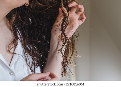 Close-up of feminine hand holding a strand of her wavy hair. Styling with curly method - Shutterstock ID 2210816061