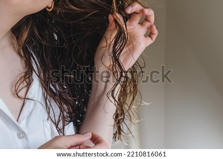 Close-up of feminine hand holding a strand of her wavy hair. Styling with curly method