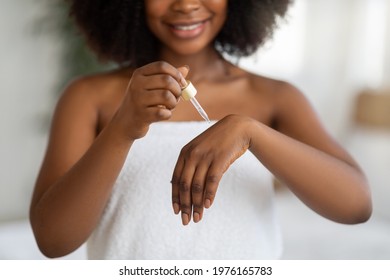 Closeup of feminine young black lady applying regenerating serum on her hands at home. Cropped view of millennial African American woman pampering herself, using skin elixir indoors - Shutterstock ID 1976165783