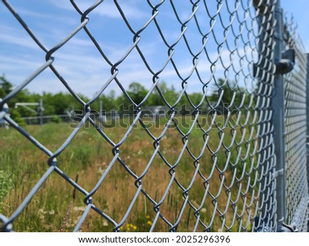 A closeup of a fence that is protecting a property. The metal gate is a chain link fence with barbed wire at the very top of it.